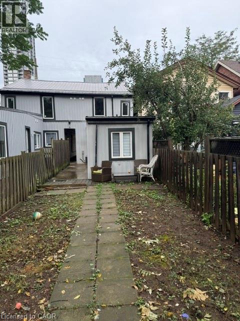 Rear yard featuring a paved stone walkway, vertical board siding, metal roof, and wood privacy fencing - 197 Ferguson Avenue S, Hamilton, ON