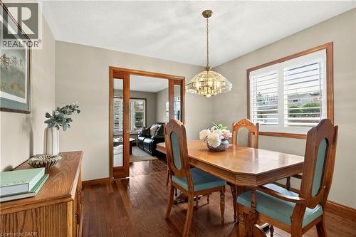 Dining area featuring wood-finish flooring, wood-framed sliding glass pocket doors, plantation shutters, and a decorative multi-bulb pendant light fixture - 53 Bastille Street, Hamilton, ON 