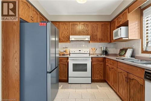 Kitchen featuring oak cabinetry, ceramic tile flooring, stainless steel French door refrigerator, white freestanding range, and built-in microwave - 53 Bastille Street, Hamilton, ON 