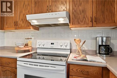 Kitchen featuring wood cabinetry, white electric range with a glass cooktop, matching range hood with integrated lighting, and a square-tile backsplash - 53 Bastille Street, Hamilton, ON 
