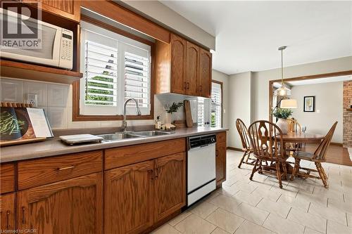 Kitchen featuring oak cabinetry, solid surface countertops, a stainless steel dual-basin sink, an integrated microwave, and tile flooring - 53 Bastille Street, Hamilton, ON 