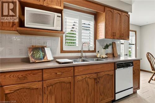 Kitchen featuring wood cabinetry, integrated microwave, dual-basin stainless steel sink with pull-down faucet, tile backsplash, and dishwasher - 53 Bastille Street, Hamilton, ON 