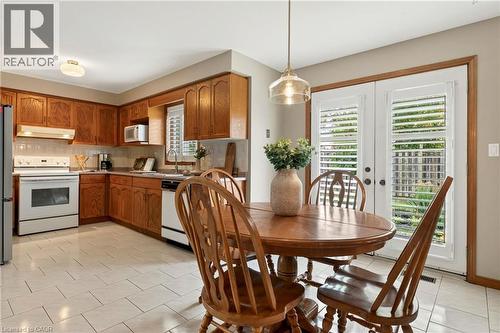 Kitchen featuring wood cabinetry, white tile flooring, integrated white appliances, and glass-paneled double doors with interior shutters - 53 Bastille Street, Hamilton, ON 