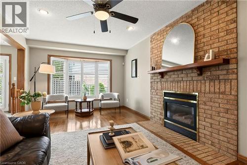 Floor-to-ceiling brick fireplace with a wood mantel, recessed lighting, ceiling fan, bay window with plantation shutters, and wood-finish flooring - 53 Bastille Street, Hamilton, ON 