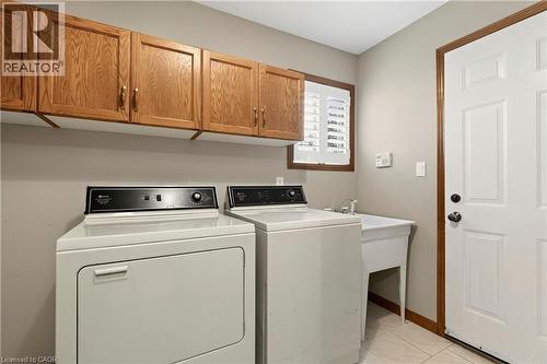 Laundry area featuring wood cabinetry, white utility sink, and window with shutters - 53 Bastille Street, Hamilton, ON 