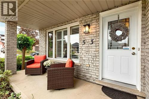 Covered front porch featuring a light-toned brick facade, white door with glass detailing, and exterior wall-mounted lantern lighting - 53 Bastille Street, Hamilton, ON 