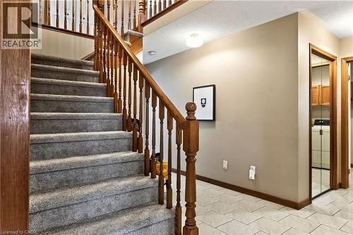 Staircase featuring wood railings and newel posts, neutral wall-to-wall carpeting, light-toned ceramic tile flooring, and a mirrored closet door - 53 Bastille Street, Hamilton, ON 