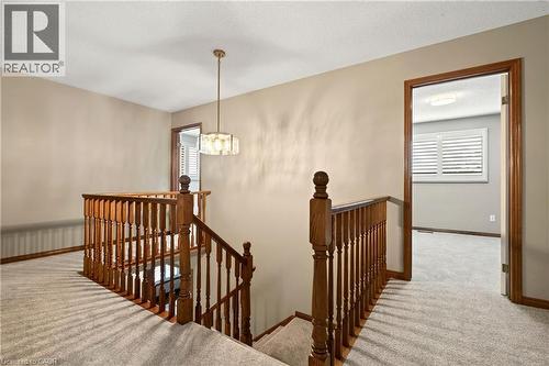 Staircase featuring wood railings and turned newel posts, complemented by a tiered multi-light pendant fixture, neutral carpeting, and interior wood-framed doorways with louvered shutters - 53 Bastille Street, Hamilton, ON 