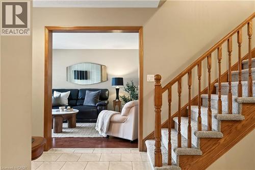 Foyer featuring ceramic tile flooring, wood-finish staircase with matching handrail and balusters, carpeted stair treads, and a wide interior doorway with wood-finish trim - 53 Bastille Street, Hamilton, ON 