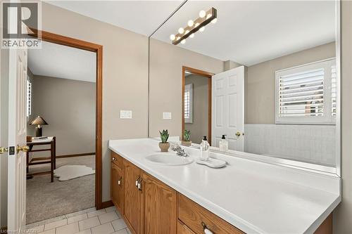 Full-width vanity with white integrated sink and countertop, wood-finish cabinetry, expansive wall-mounted mirror, multi-bulb vanity lighting, and white wall tile surround - 53 Bastille Street, Hamilton, ON 