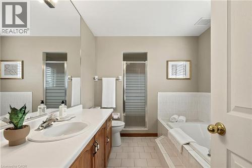 Bathroom featuring a vanity with an integrated countertop, full-width mirror, shower enclosure with frosted glass, and a tiled tub surround - 53 Bastille Street, Hamilton, ON 