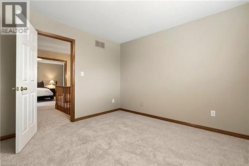 Neutral-toned interior space featuring carpeting, a six-panel white door, and wood-trim door casing - 53 Bastille Street, Hamilton, ON 
