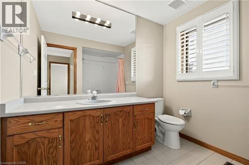 Bathroom featuring wood cabinetry, a solid surface countertop with integrated sink, a full-width mirror, and window shutters - 53 Bastille Street, Hamilton, ON 