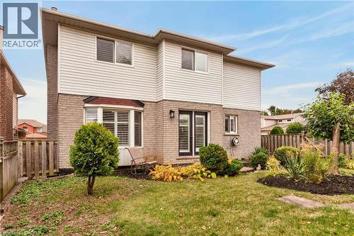 Two-story exterior featuring light-toned brick and horizontal siding, double-pane bay window, and glass-paneled double exterior doors, set within a fenced backyard with landscaped garden beds - 53 Bastille Street, Hamilton, ON 
