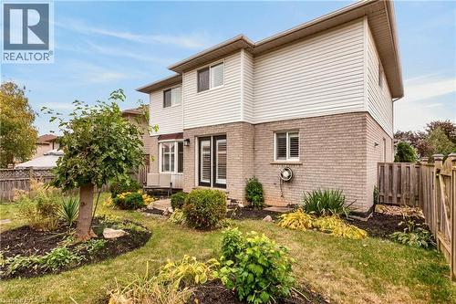 Two-story residence with a brick and light-colored siding exterior, featuring double glass-paneled doors, landscaped garden beds, and a wood privacy fence - 53 Bastille Street, Hamilton, ON 