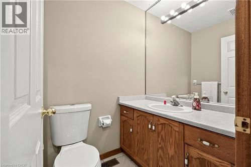 Bathroom vanity featuring wood-finish cabinetry, an integrated oval sink, stone-composite countertop, full-width wall mirror, and multi-bulb vanity light fixture - 53 Bastille Street, Hamilton, ON 