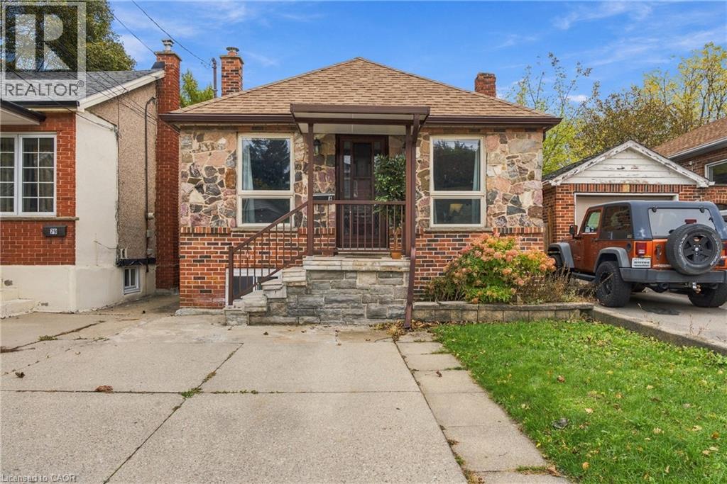 Exterior featuring stone and brick facade, gabled roof, concrete driveway, and covered front porch with metal railings - 81 East 23Rd Street, Hamilton, ON