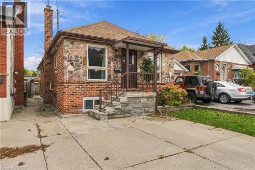 Exterior facade featuring mixed-material stone and brick masonry, covered front entryway with metal railings, and private concrete driveway - 81 East 23Rd Street, Hamilton, ON 