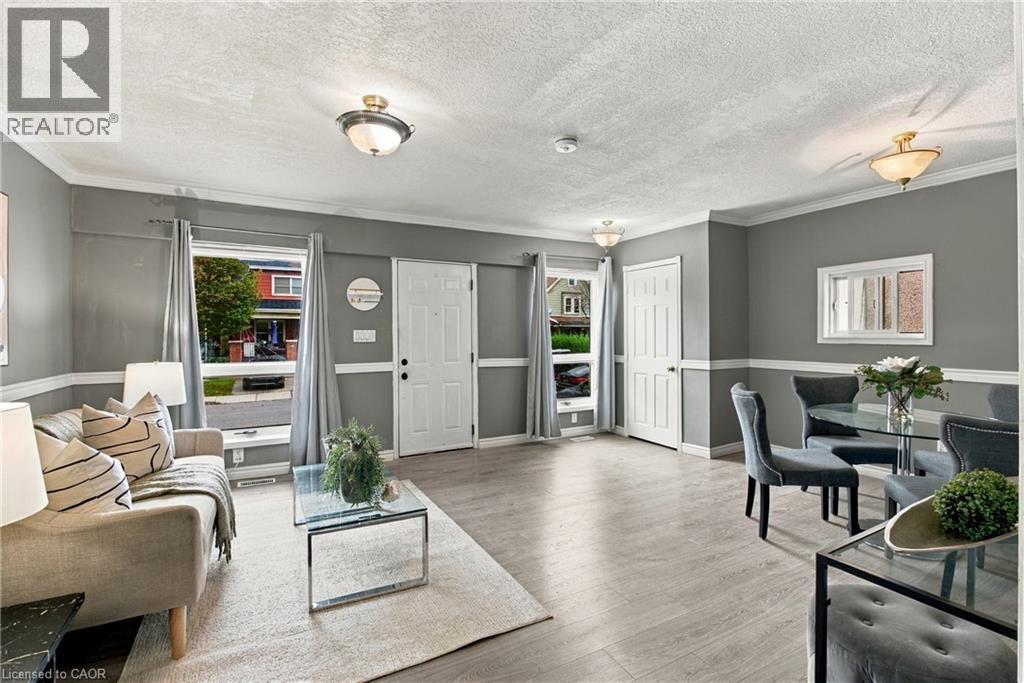 Open-concept area featuring wood-finish flooring, crown molding, chair rail trim, multiple flush-mount ceiling light fixtures, and windows with neutral-tone window treatments - 81 East 23Rd Street, Hamilton, ON