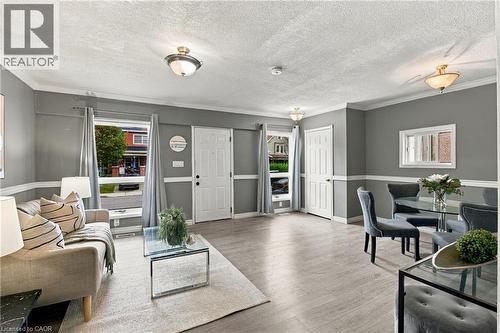 Open-concept area featuring wood-finish flooring, crown molding, chair rail trim, multiple flush-mount ceiling light fixtures, and windows with neutral-tone window treatments - 81 East 23Rd Street, Hamilton, ON 