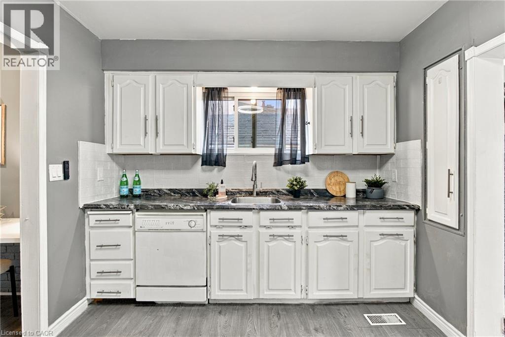 Kitchen featuring white shaker-style cabinetry, dark stone-patterned countertops, a stainless steel undermount sink with a gooseneck faucet, a built-in dishwasher, and wood-finish flooring - 81 East 23Rd Street, Hamilton, ON
