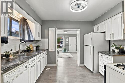 Kitchen featuring white cabinetry, dark stone-pattern countertops, a stainless steel undermount sink with a gooseneck faucet, wood-finish flooring, and a circular LED flush-mount fixture - 81 East 23Rd Street, Hamilton, ON 
