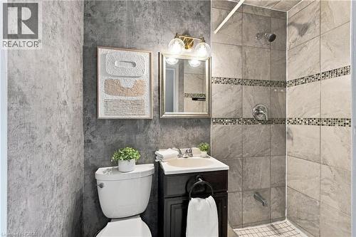 Bathroom featuring a dark wood-finish vanity, stone-patterned wall tile, glass mosaic tile accents, a metallic wall-mounted light fixture, and a built-in tub and shower combination - 81 East 23Rd Street, Hamilton, ON 