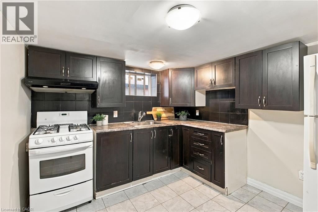 Kitchen featuring dark-toned cabinetry, stone-finish countertops, black tile backsplash, and ceramic tile flooring - 81 East 23Rd Street, Hamilton, ON