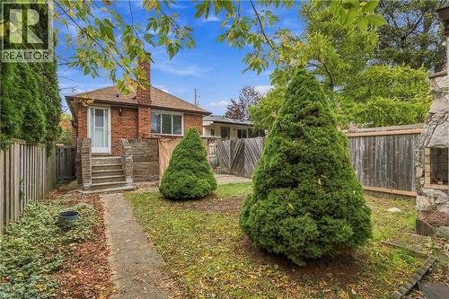 Brick exterior featuring a masonry chimney, concrete steps, a stone-faced outdoor hearth, and wood perimeter fencing - 81 East 23Rd Street, Hamilton, ON 
