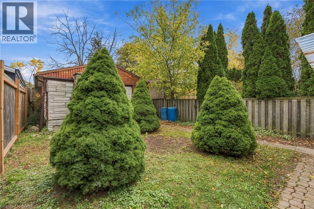 Backyard featuring mature evergreen trees, stone-textured exterior siding, perimeter wood fencing, and a paver stone walkway - 81 East 23Rd Street, Hamilton, ON
