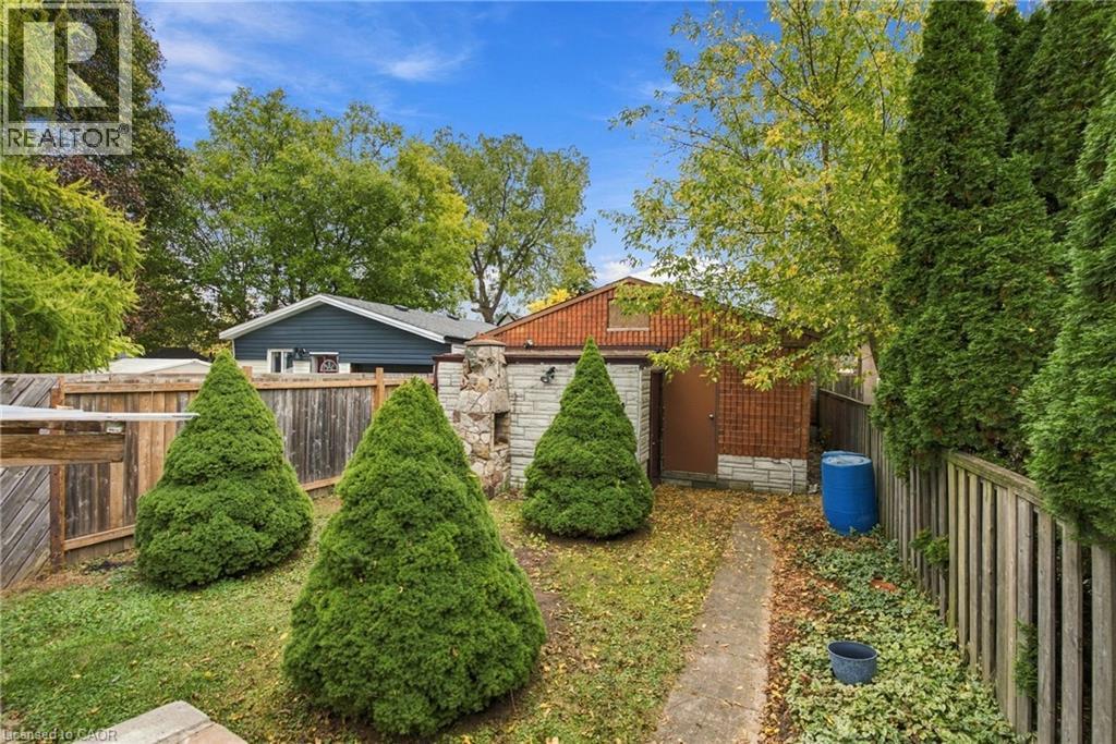 Outdoor space featuring a masonry fireplace, a wood fence, and mature evergreen landscaping - 81 East 23Rd Street, Hamilton, ON