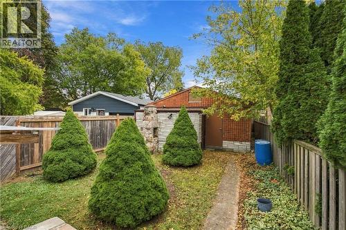 Outdoor space featuring a masonry fireplace, a wood fence, and mature evergreen landscaping - 81 East 23Rd Street, Hamilton, ON 
