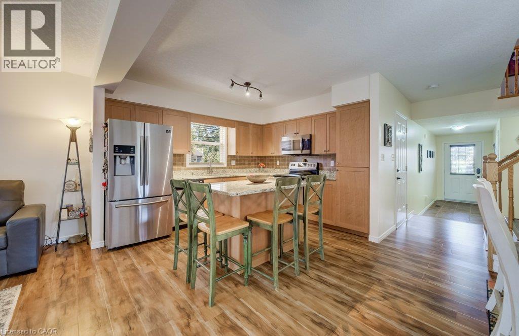Kitchen featuring light-finish cabinetry, stone-surfaced countertops, a center island with seating space, stainless steel appliances, and wood-finish flooring - 521 Snowdrop Court, Kitchener, ON