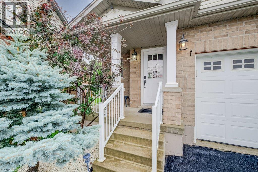 Exterior entrance featuring brick cladding, a covered porch with column supports, white railings, and a single-car garage with rectangular inset windows - 521 Snowdrop Court, Kitchener, ON