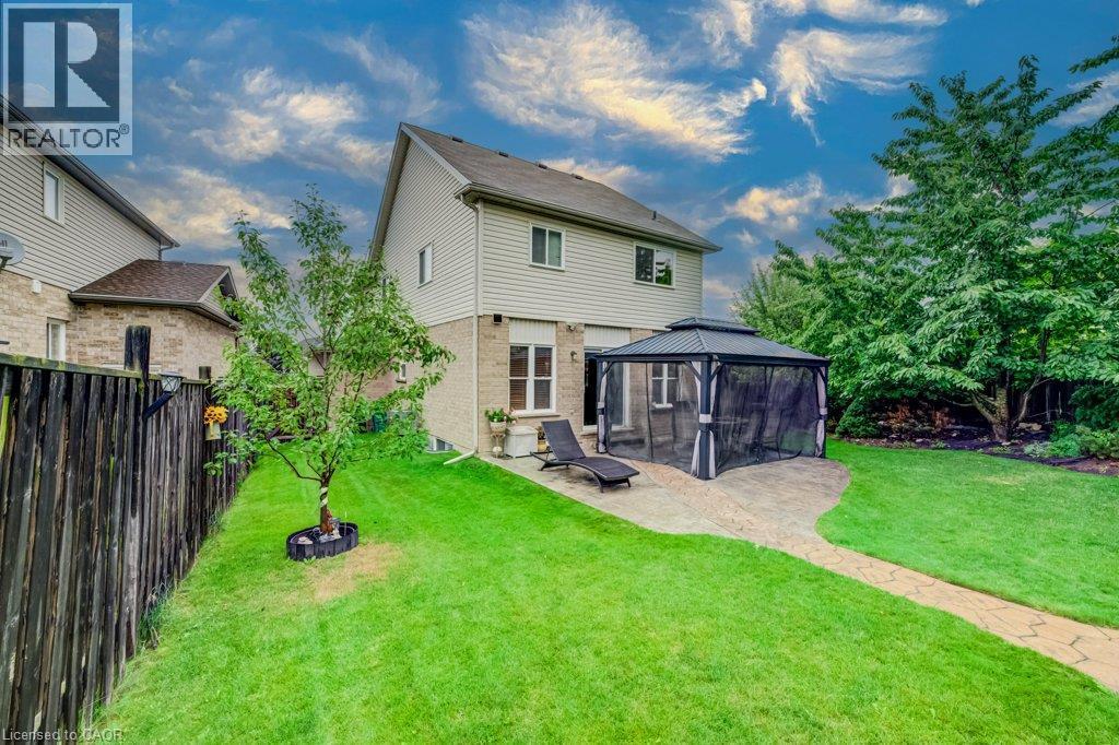 Rear exterior featuring a brick and vinyl siding facade, stone-paver patio, metal-framed gazebo, and enclosed perimeter fencing - 521 Snowdrop Court, Kitchener, ON