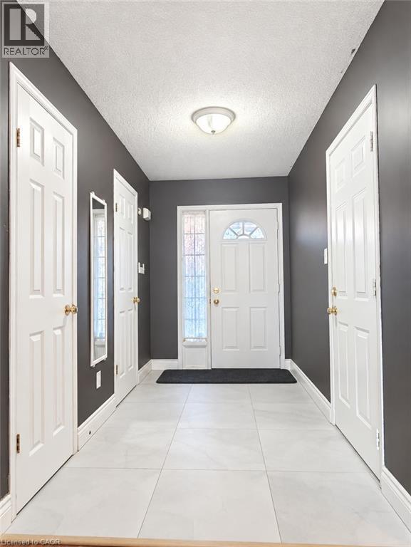 Entryway featuring large-format light tile flooring, white six-panel interior doors, and a front entry door with a decorative glass sidelight and transom window - 52 Isabella Street, Kitchener, ON