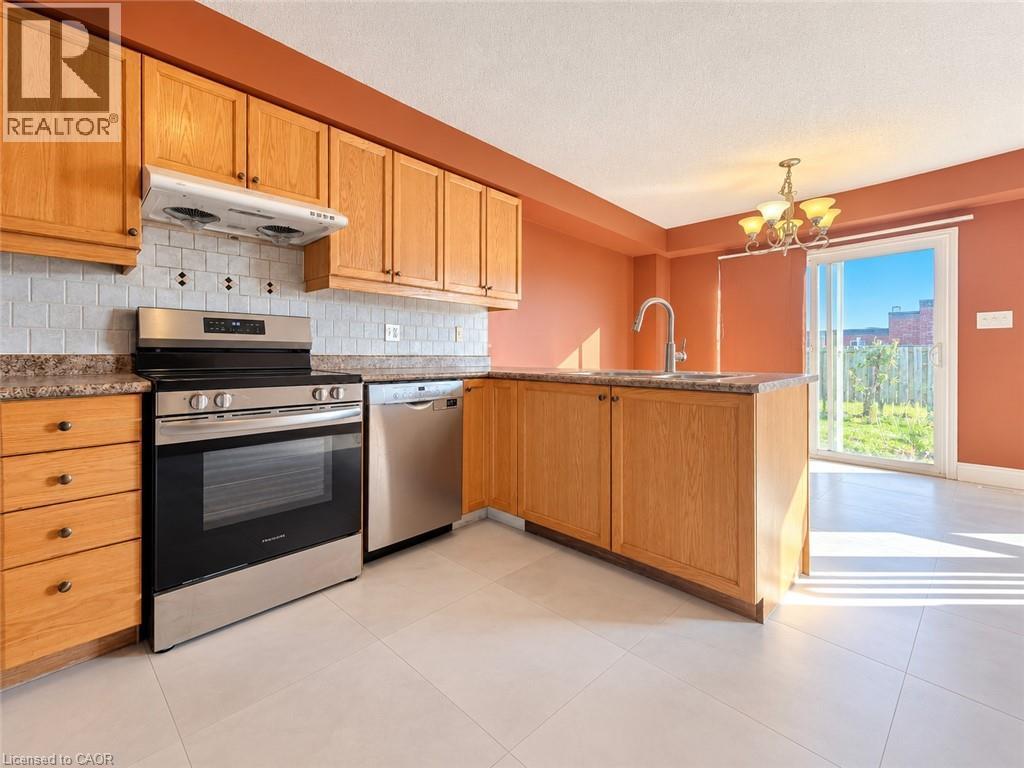 Kitchen featuring natural wood cabinetry, stainless steel appliances, a tile backsplash, light-toned flooring, and a glass sliding door - 52 Isabella Street, Kitchener, ON