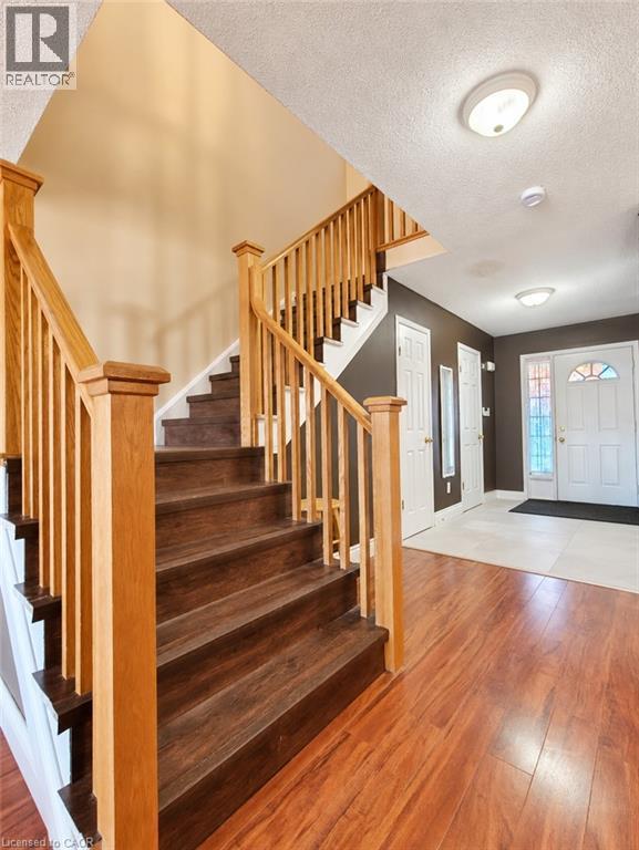 Foyer entry featuring wood-finish flooring, a staircase with light wood railing and balusters, and a solid-core front door with decorative glass paneling - 52 Isabella Street, Kitchener, ON