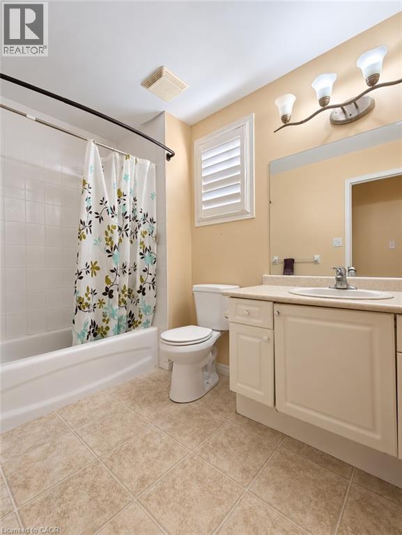 Bathroom featuring a white vanity cabinet with a composite countertop, integrated sink basin, large wall-mounted mirror, three-light fixture, and ceramic tile flooring - 52 Isabella Street, Kitchener, ON