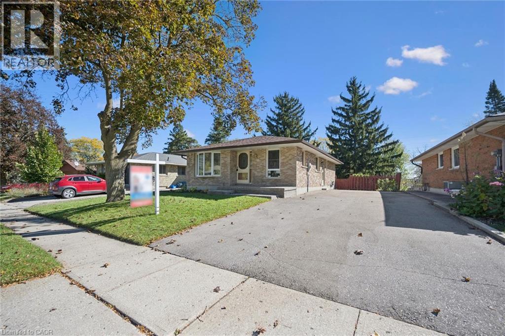 Brick exterior featuring a multi-pane bay window, low-pitched roofline, asphalt driveway, and mature trees - 11 Caledon Court, Cambridge, ON