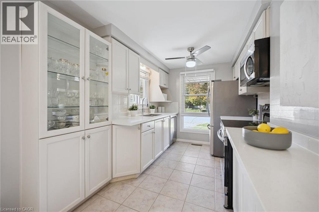 Kitchen featuring white cabinetry with glass-front display uppers, solid-surface countertops, tile flooring, stainless steel appliances, and a ceiling fan - 11 Caledon Court, Cambridge, ON