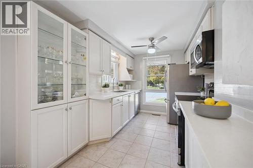 Kitchen featuring white cabinetry with glass-front display uppers, solid-surface countertops, tile flooring, stainless steel appliances, and a ceiling fan - 11 Caledon Court, Cambridge, ON 