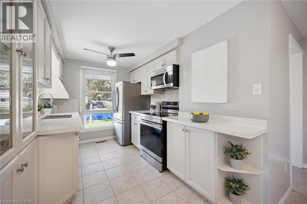 Kitchen featuring white cabinetry, solid-surface countertops, stainless steel appliances, ceramic tile flooring, and a ceiling-mounted light fixture - 11 Caledon Court, Cambridge, ON