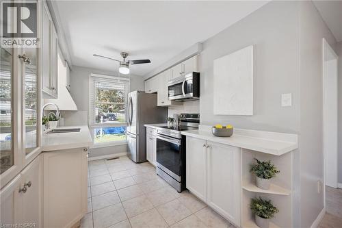 Kitchen featuring white cabinetry, solid-surface countertops, stainless steel appliances, ceramic tile flooring, and a ceiling-mounted light fixture - 11 Caledon Court, Cambridge, ON 