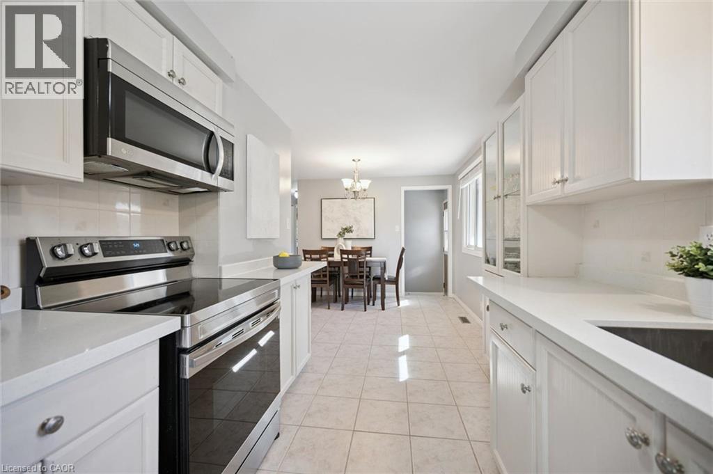 Kitchen featuring white shaker-style cabinetry, solid-surface countertops, tile flooring, and stainless steel appliances - 11 Caledon Court, Cambridge, ON