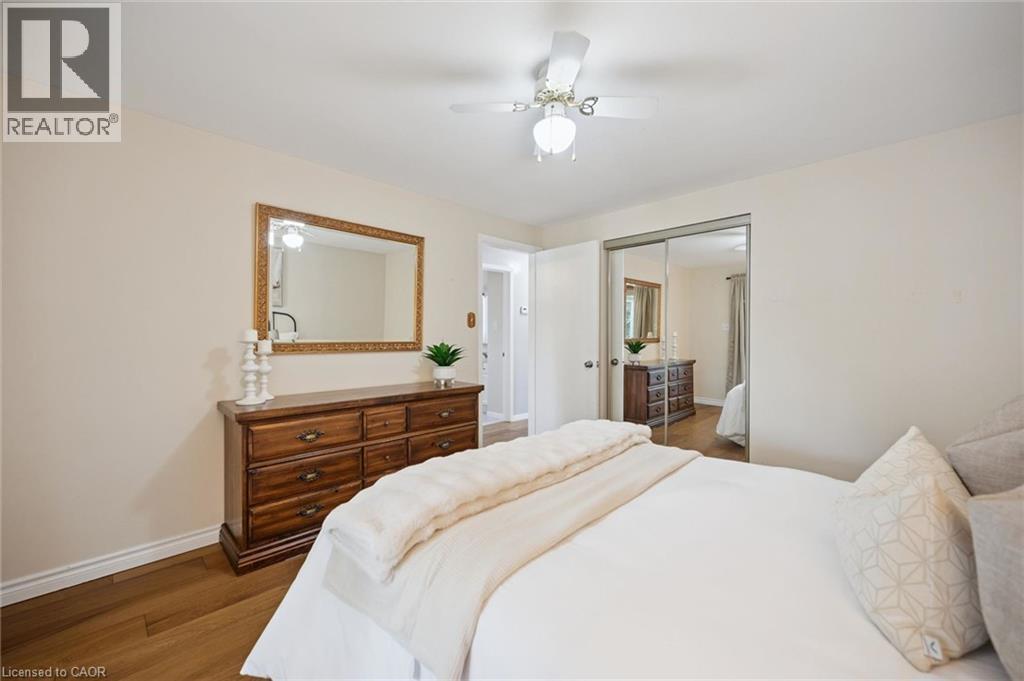 Room featuring wood-finish flooring, a ceiling fan with integrated lighting, and mirrored sliding closet doors - 11 Caledon Court, Cambridge, ON