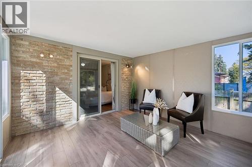 Enclosed sunroom featuring exposed brick accent walls, wood-finish flooring, sliding glass door, and large picture windows - 11 Caledon Court, Cambridge, ON 
