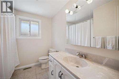Bathroom featuring a vanity with integrated sink, stone-finish countertop, three-panel mirrored medicine cabinet, multi-light fixture, and tile flooring - 11 Caledon Court, Cambridge, ON 