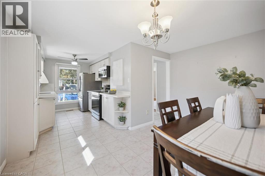 Kitchen featuring white cabinetry with open shelving, stainless steel appliances, ceramic tile flooring, and a decorative multi-bulb chandelier - 11 Caledon Court, Cambridge, ON