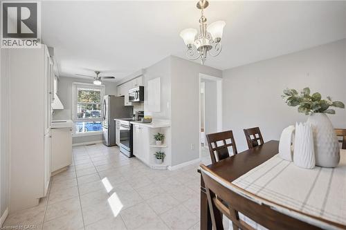 Kitchen featuring white cabinetry with open shelving, stainless steel appliances, ceramic tile flooring, and a decorative multi-bulb chandelier - 11 Caledon Court, Cambridge, ON 